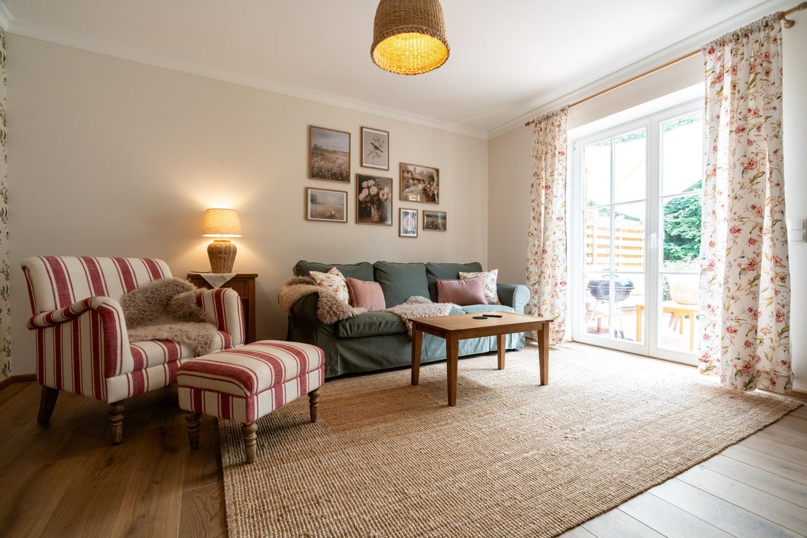 Wohnzimmer mit Sofa, Sessel, Tisch und Fenster zur Terrasse.