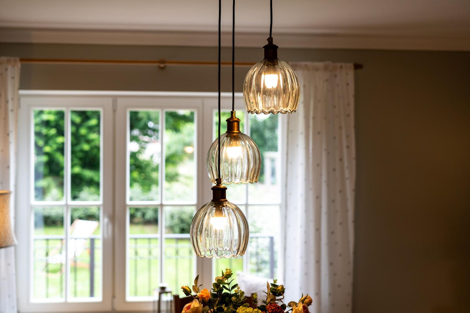 Drei hängende Lampen mit Glasgehäusen über einem Tisch mit Blumen