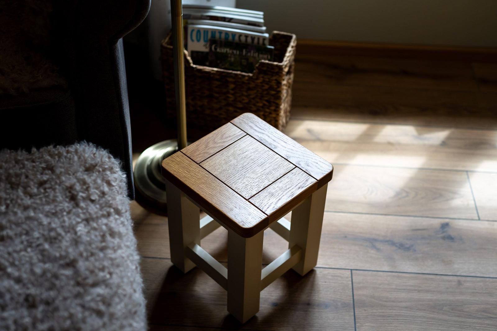 Holzstuhl mit quadratischer Sitzfläche auf Holzboden neben einem Sitzmöbel.
