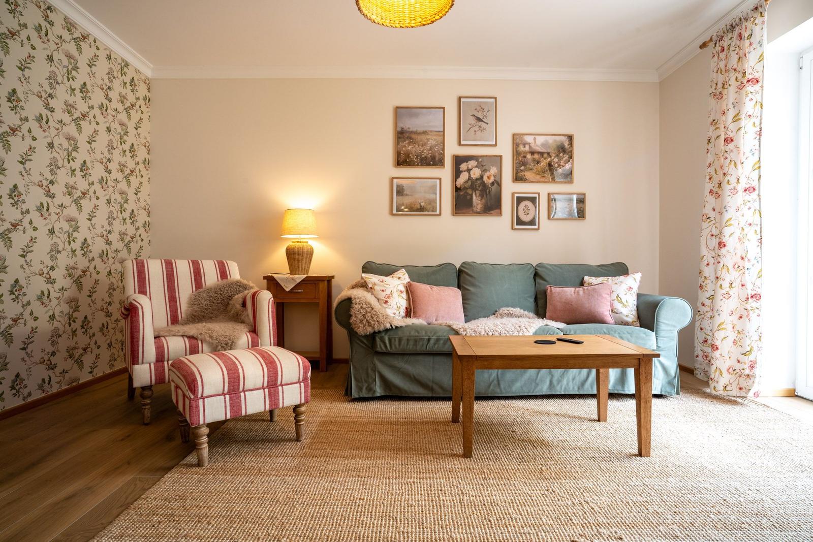Wohnzimmer mit Sofa, Sessel, Tisch und Wandbildern.