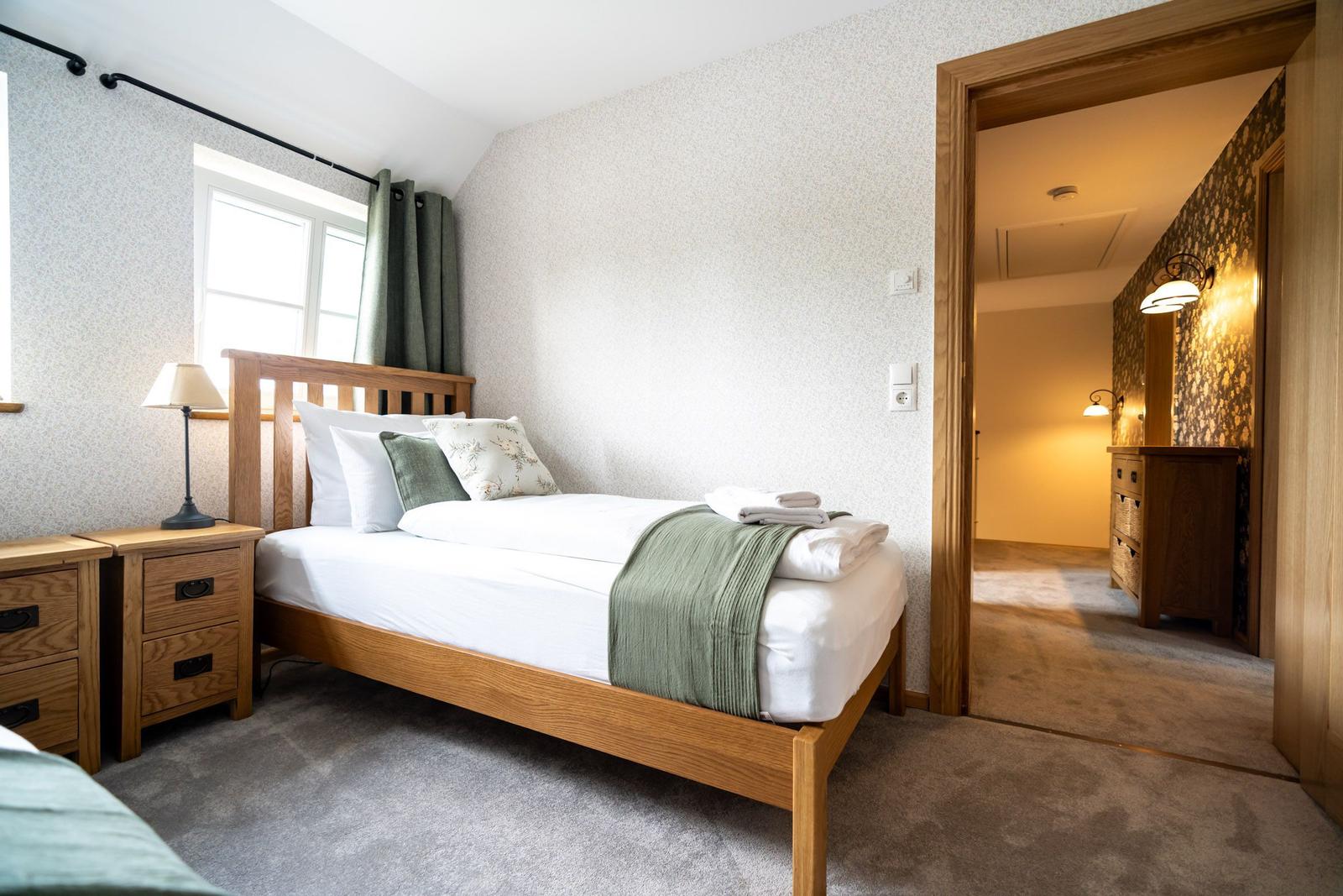 Ein Schlafzimmer mit Holzbett, Nachttisch und Fenster. Durchgang zu Badezimmer.