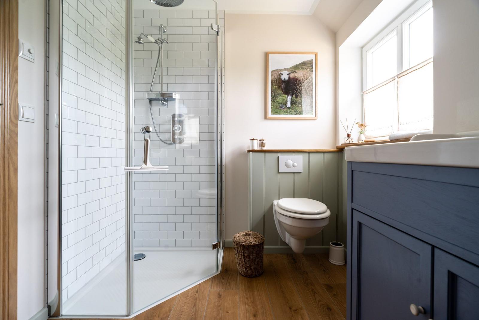 Bad mit Dusche, Toilette und Waschbecken. Holzboden und Wandbild mit Schaf.