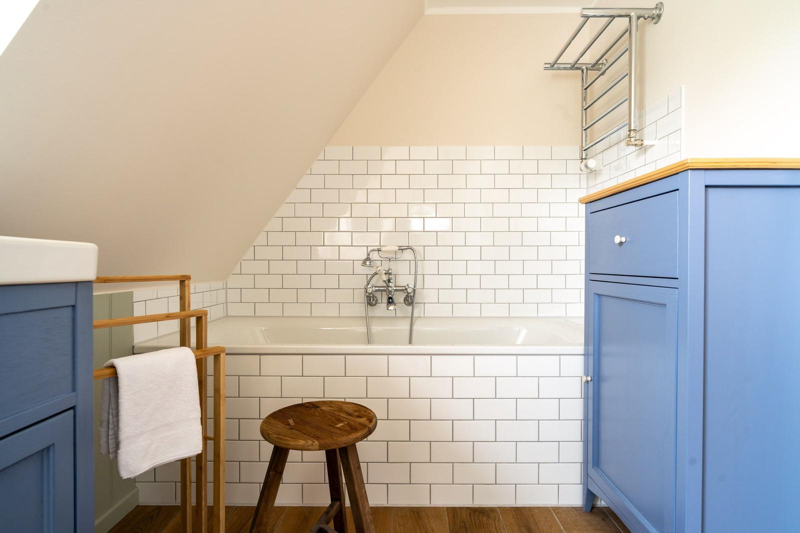 Bad mit Badewanne, weißen Fliesen und blauen Schränken unter schrägem Dach