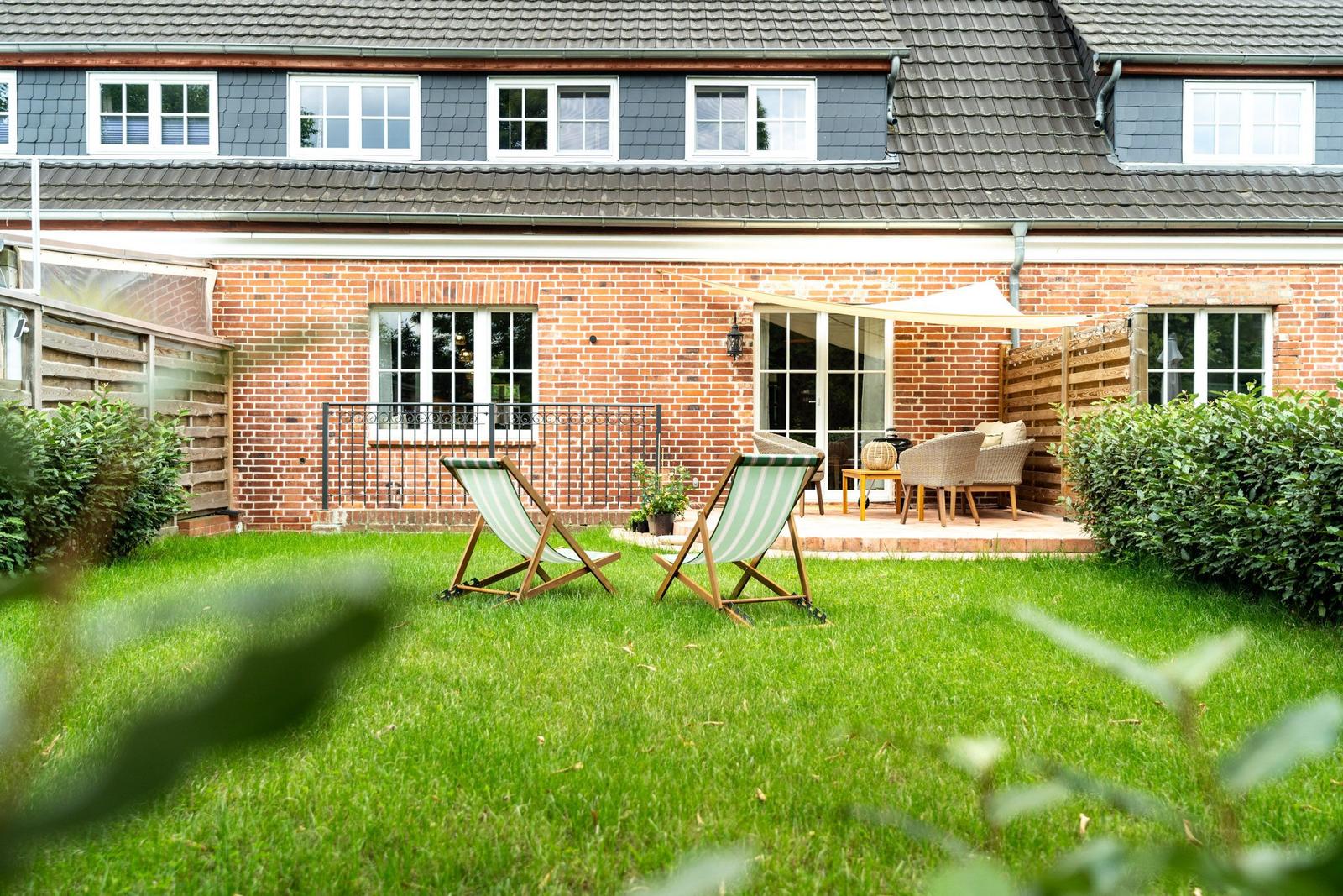 Hinterhof mit Grasfläche, zwei Liegestühlen und Terrasse mit Sitzgelegenheiten.
