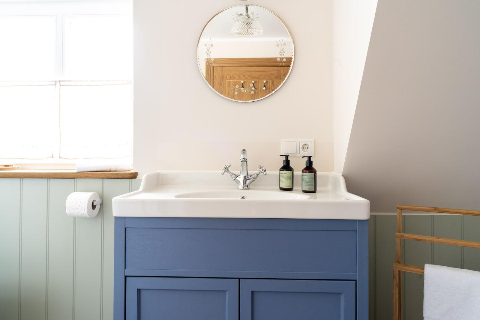 Badezimmer mit blauem Waschbecken, runden Spiegel und Holzregal.