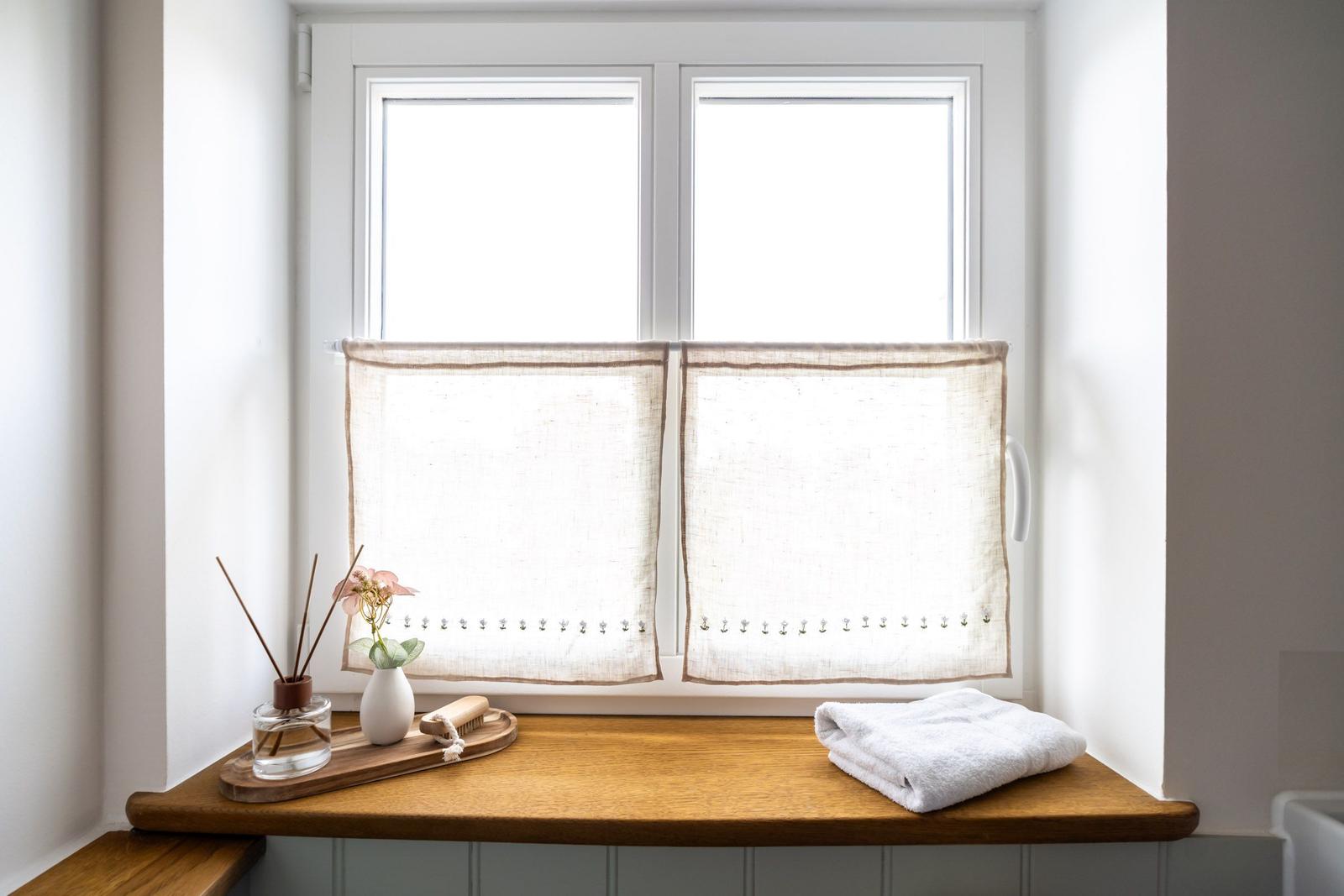 Blick aus dem Fenster mit Holzbank, weißen Vorhängen und Handtuch.