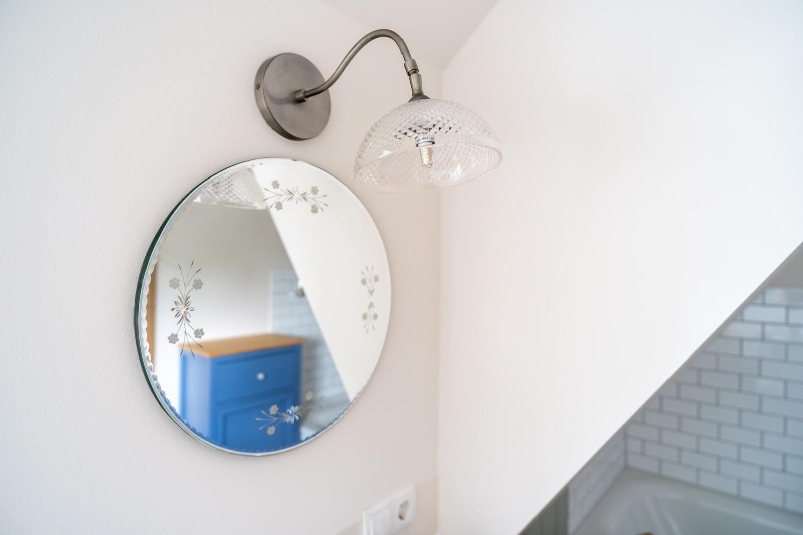 Runde Spiegelfläche mit floralen Mustern und Wandlampe mit Glasdiffusor.