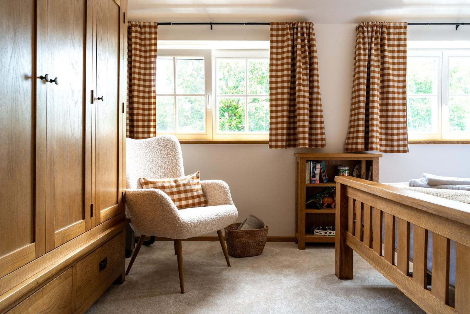 Schlafzimmer mit Holzbett, Kleiderschrank und Sessel vor Fenstern mit karierten Vorhängen.