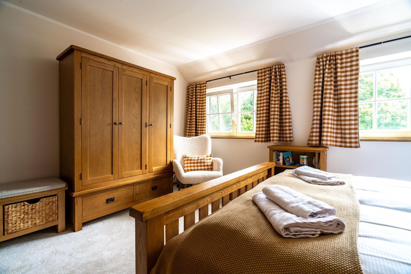 Schlafzimmer mit Holzschrank, Bett und Fenster mit Gardinen.