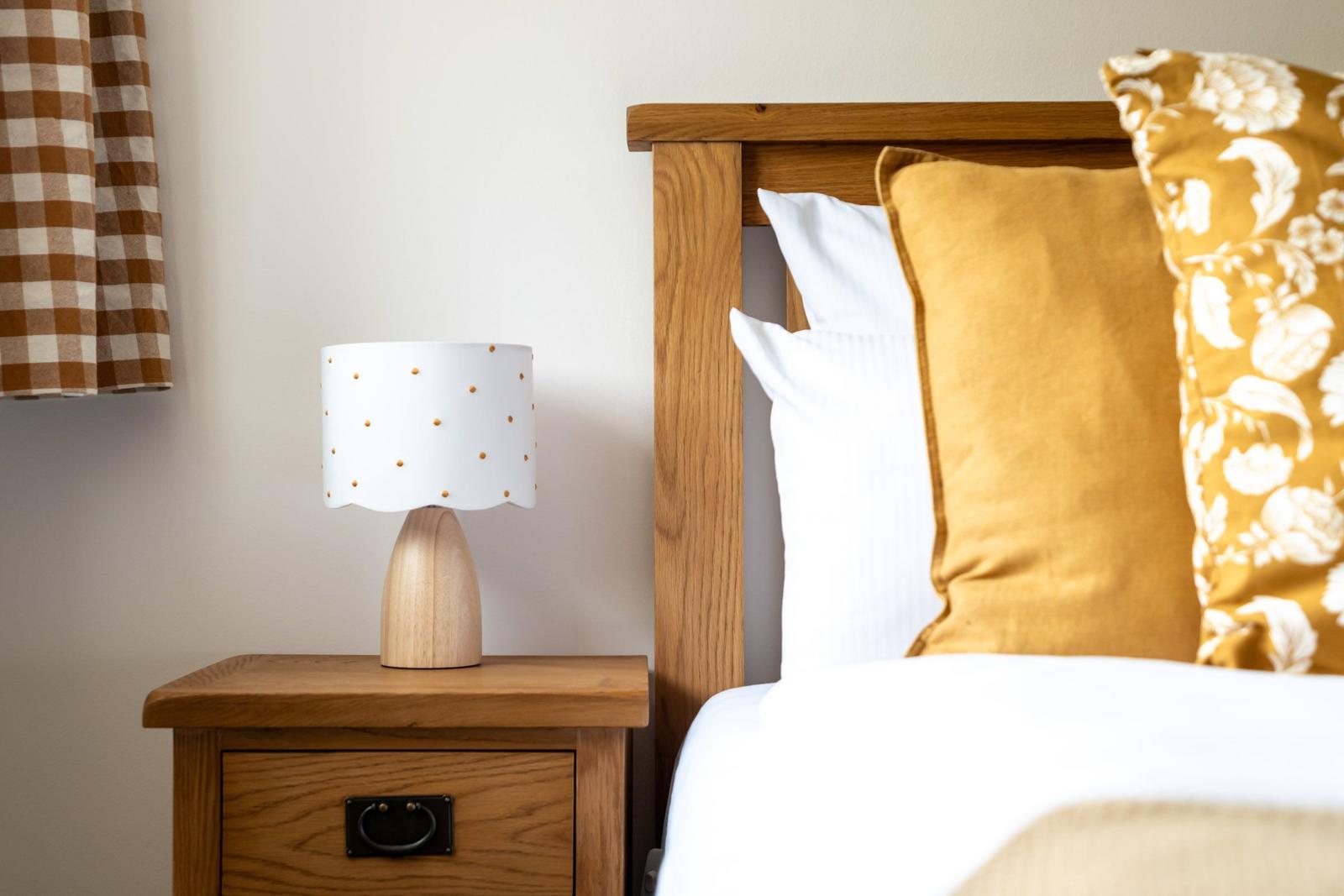 Hölzernes Nachtkästchen mit Lampe neben Bett mit Kissen.
