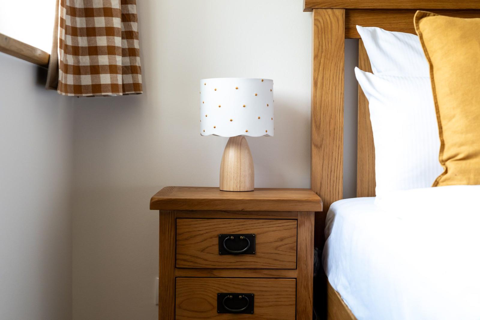 Schlafzimmer mit Holzbett, Nachttisch und Lampe mit weißem Schirm.