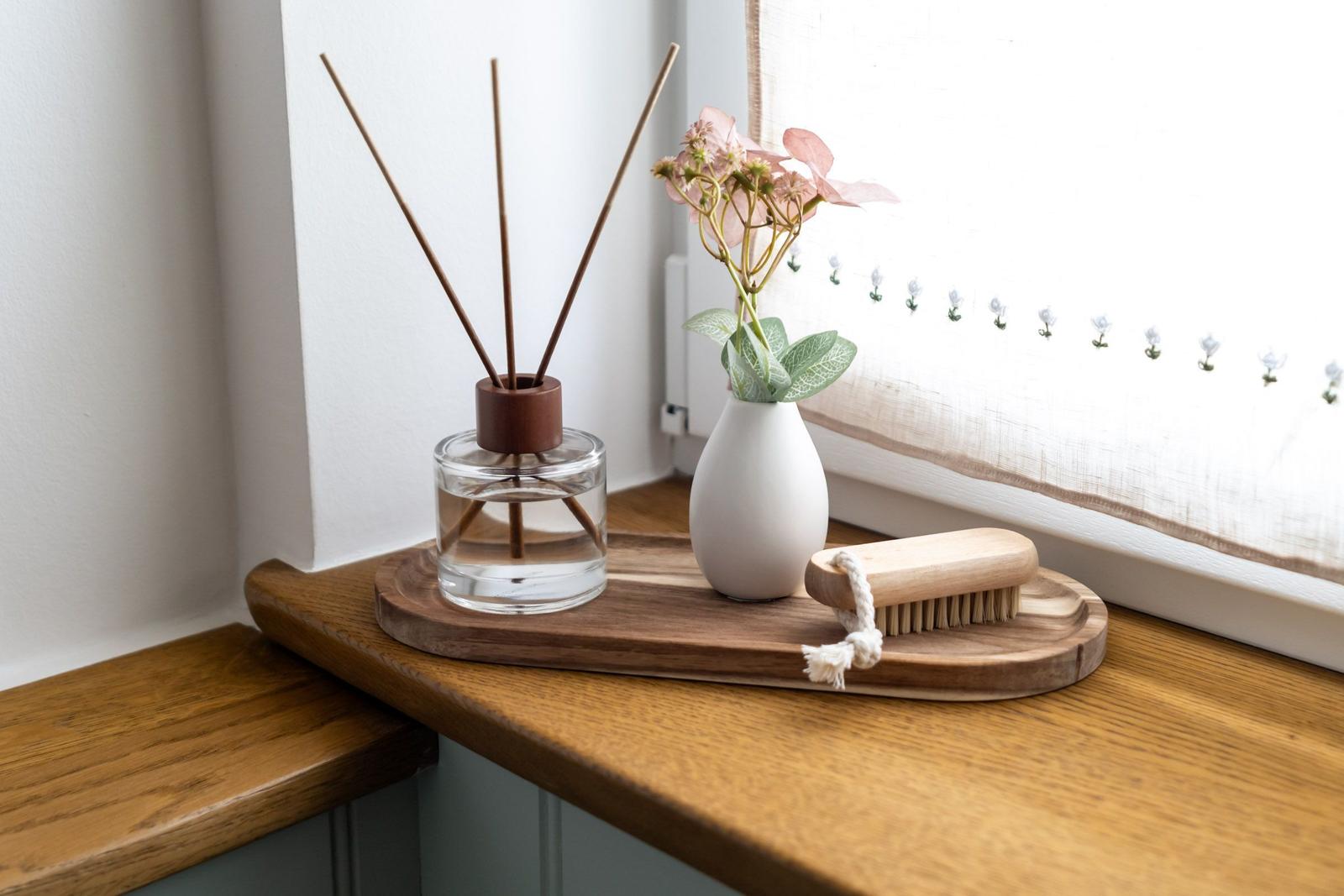 Holztablett mit Duftdiffusor, Vase und Bürste auf Fensterbank.