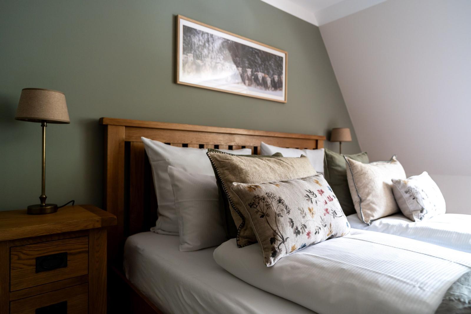 Schlafzimmer mit Holzbett, Kissen und Nachttisch. Wandbild über dem Bett.