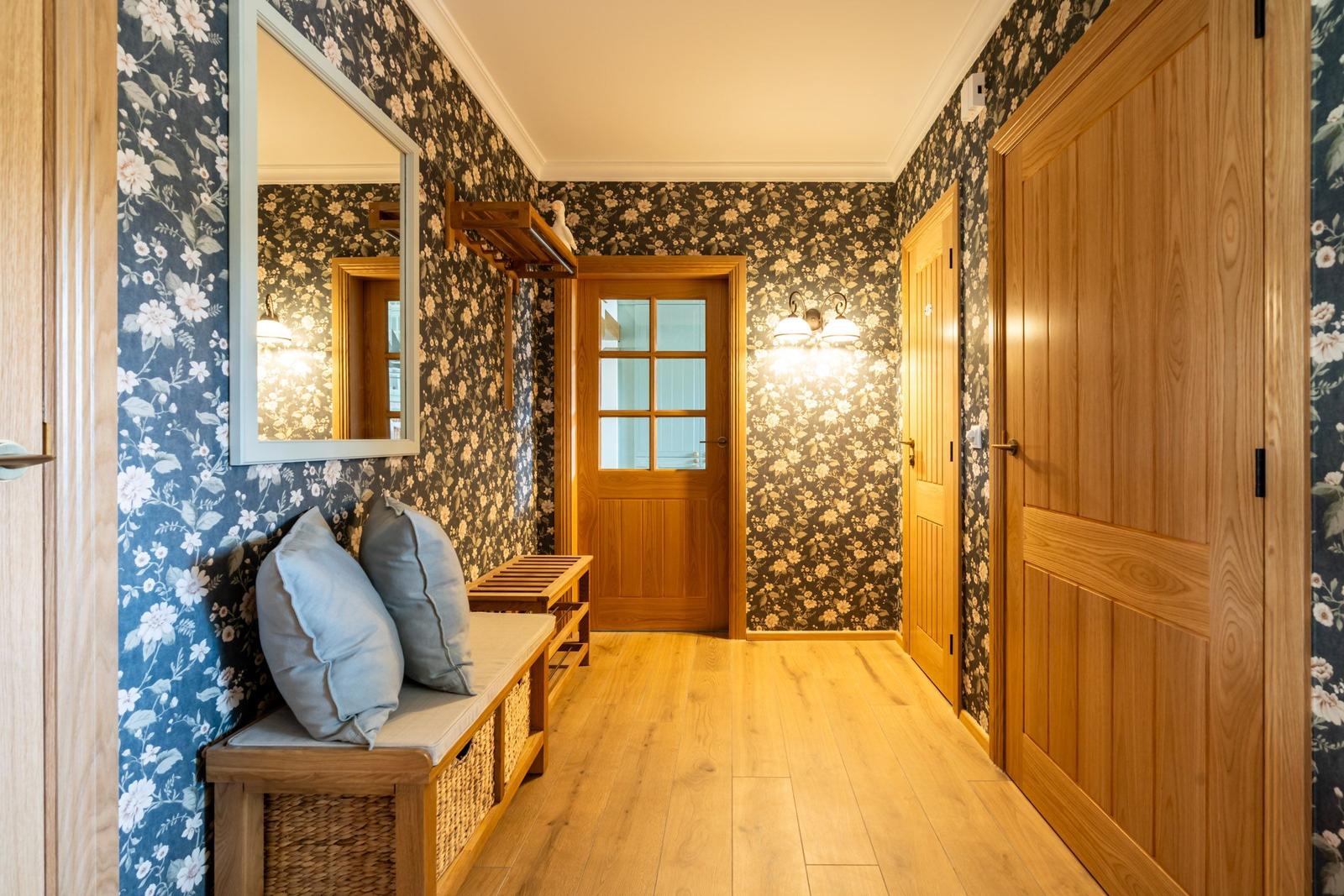 Flur mit floraler Tapete, Holztüren und Sitzbank mit Kissen.