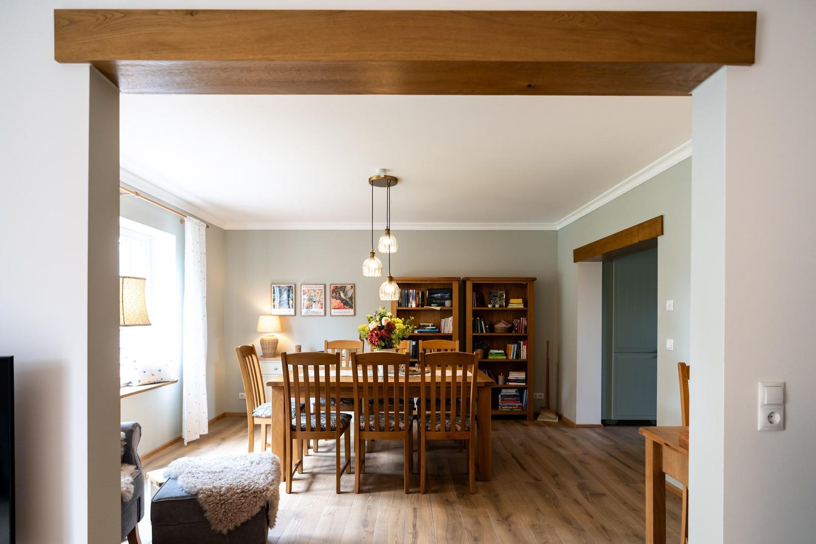Esszimmer mit Holztisch, Stühlen und Bücherregalen. Holzdeckenbalken und helle Wände.
