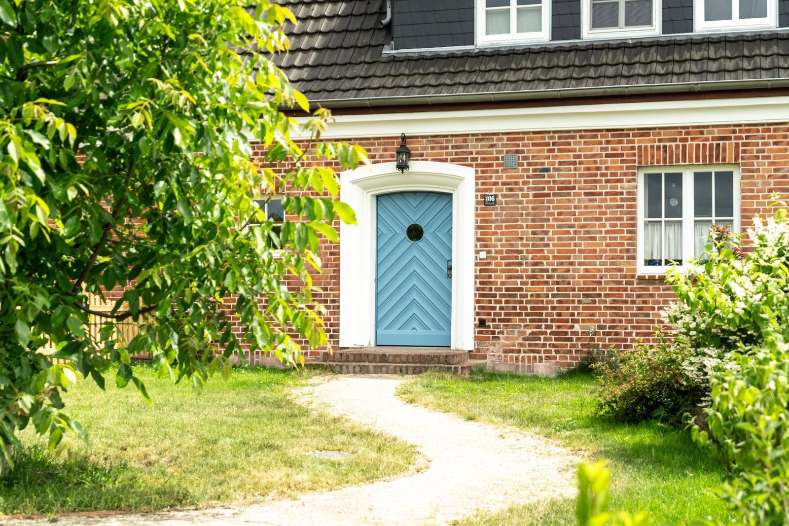 Rotes Backsteinhaus mit blauer Tür und grünem Gartenweg.