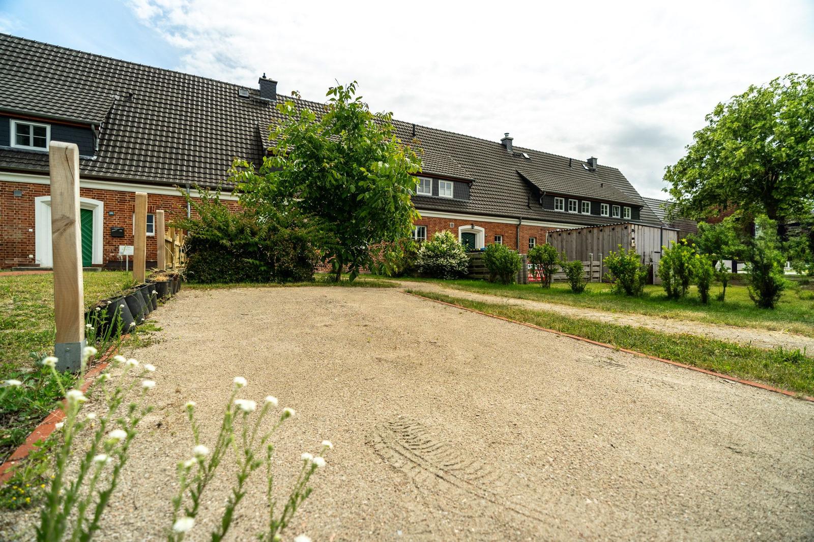 Ein langer Gartenweg führt zu einem roten Backsteinhaus mit dunklem Dach.