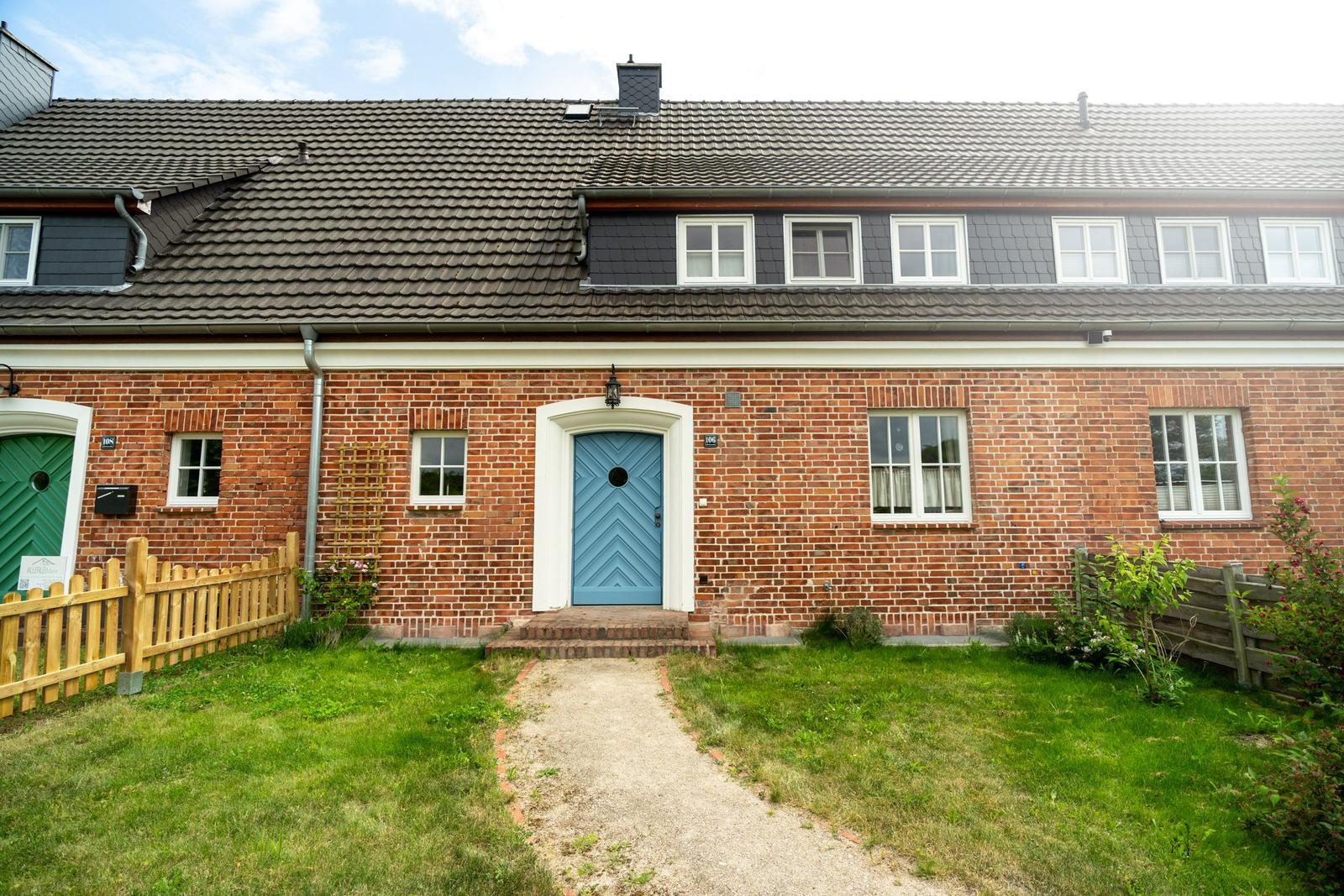 Ein Haus mit Backsteinfassade, blauer Haustür und grünem Gartenweg.