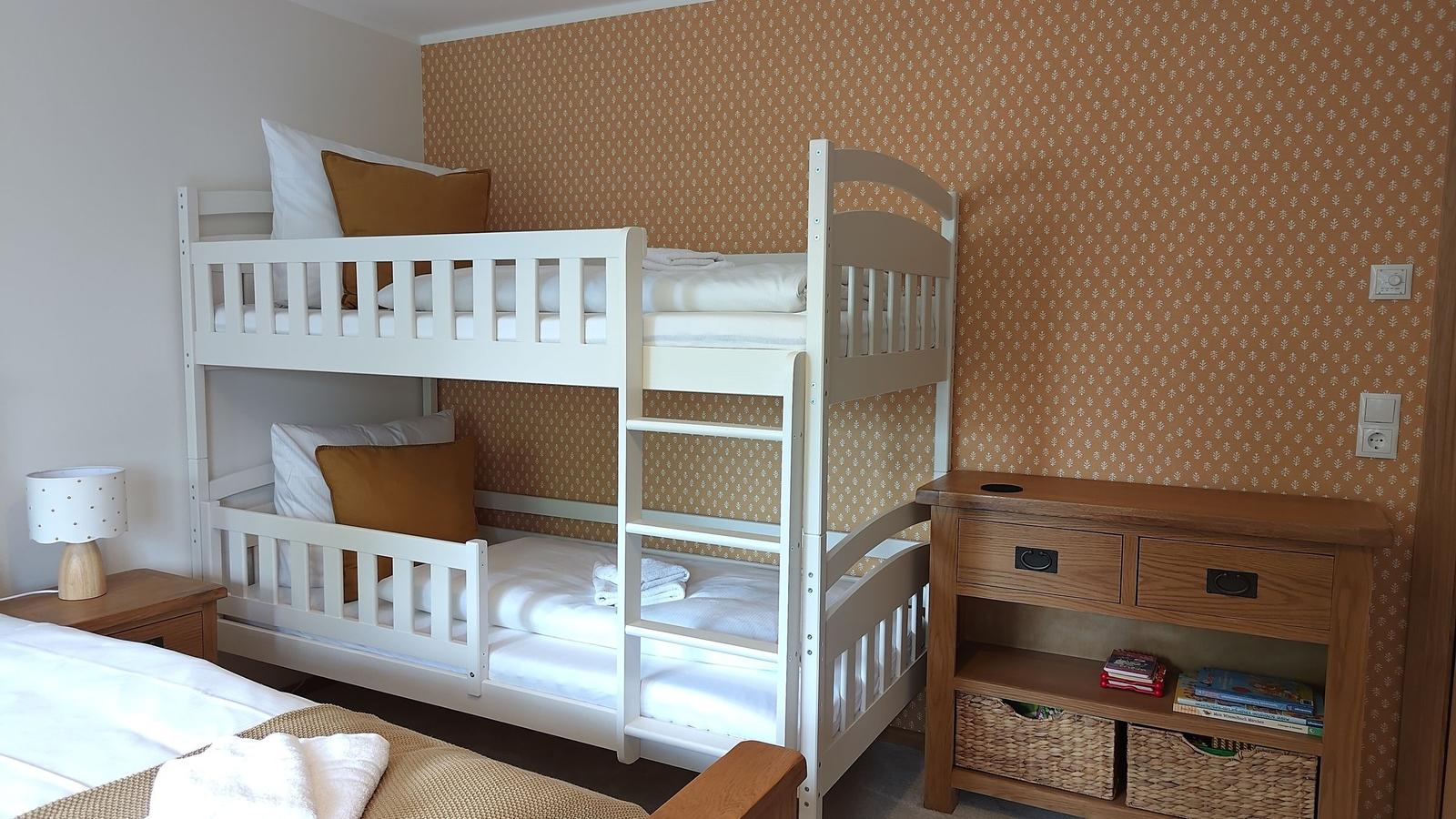 Zimmer mit Doppelstockbett, Holzkommode und gemustertem Wandbezug.
