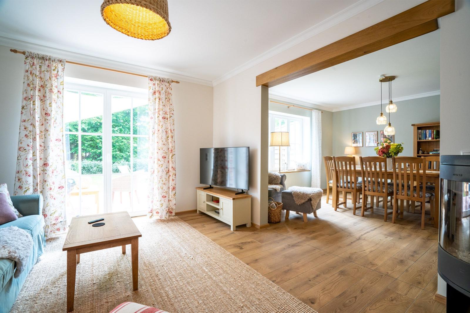 Wohn- und Essbereich mit Holzboden, TV, Tisch und Stühlen sowie Blick auf den Garten.