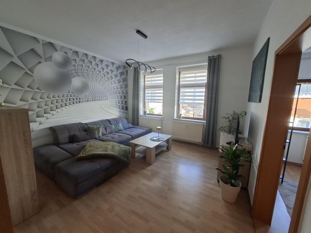 Living room with sofa, table, and windows. Wall with geometric pattern.