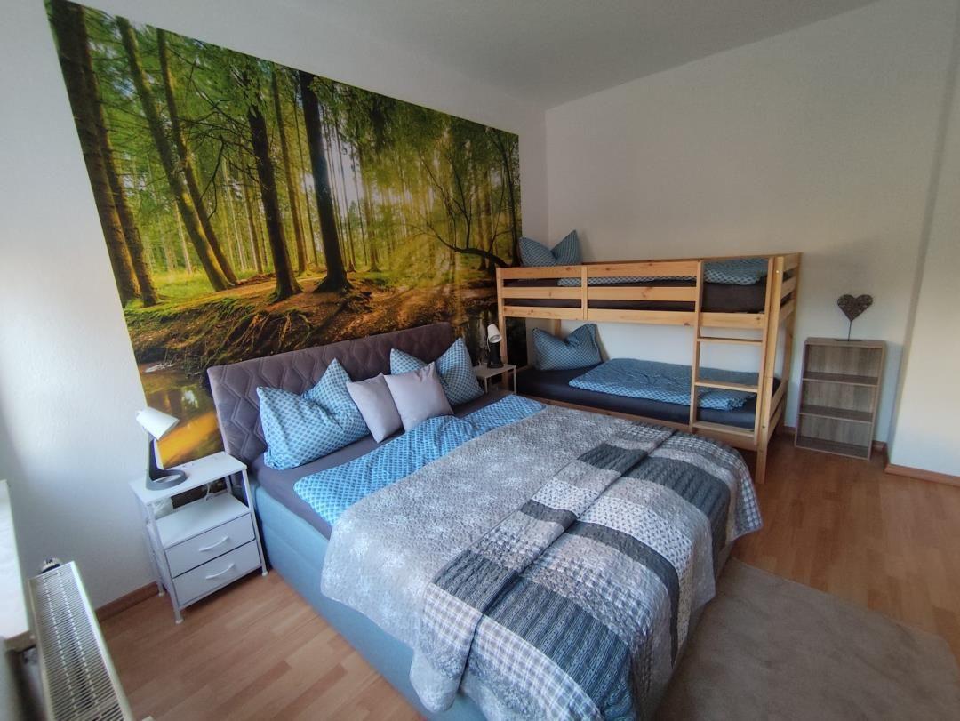 Room with double bed, bunk bed, and forest mural on the wall.