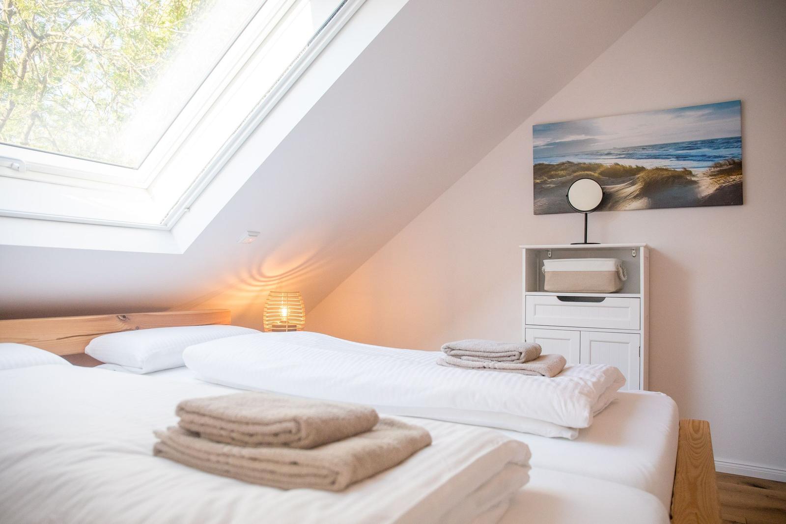 Schlafzimmer mit Dachfenster, Bett, Nachttisch und Wandbild.
