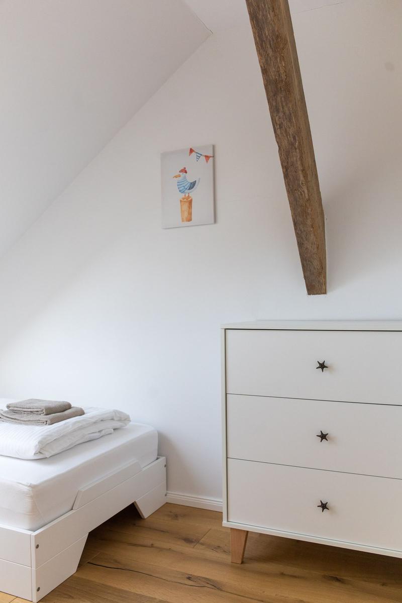 Schlafzimmer mit weißem Bett, Schrank und Holzbalken an der Wand.