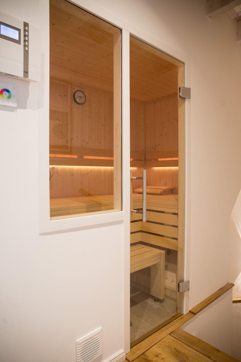 Sauna mit Holzbank und Glasfront. Temperaturanzeige an der Wand.