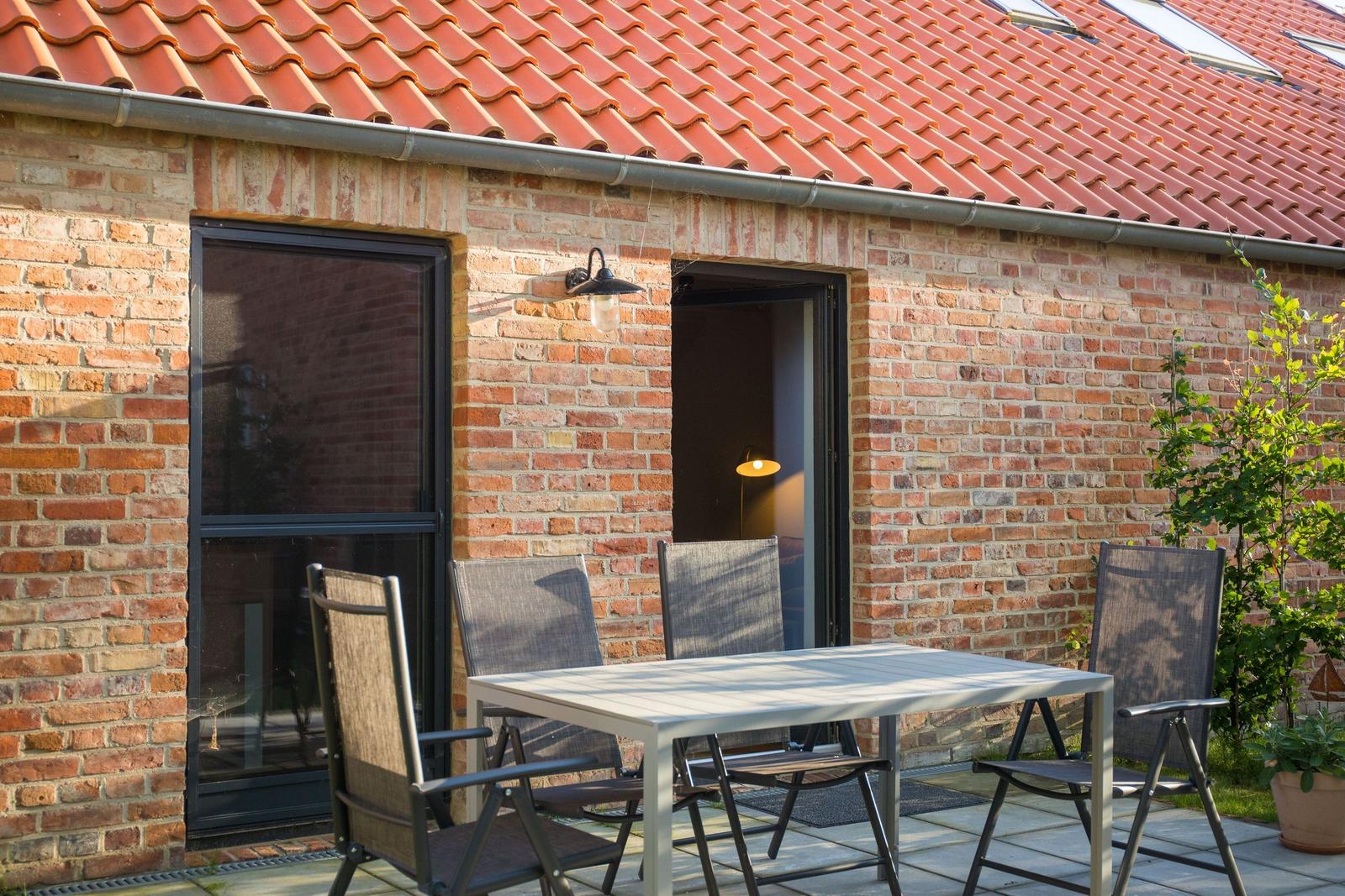 Terrasse mit Tisch und Stühlen vor Backsteinhaus mit rotem Dach