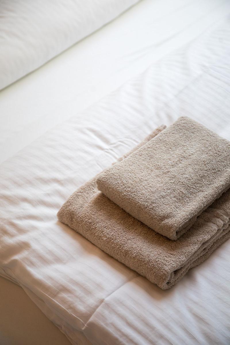 Zwei gefaltete Handtücher liegen auf einem Bett mit weißer Bettwäsche.
