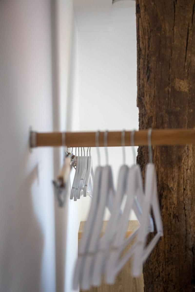 Schrank mit weißen Hängern und Holzstange, neben rustikalem Holzbaumstamm.