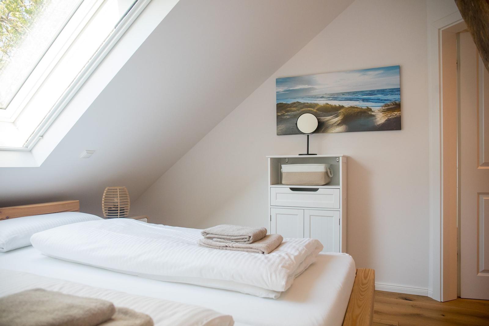 Schlafzimmer mit Dachschräge, großem Dachfenster und Bett mit weißen Laken.