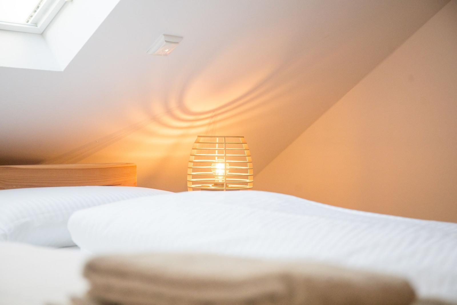 Schlafzimmer mit Dachschrägen, Bett, Lampe und Dachfenster.