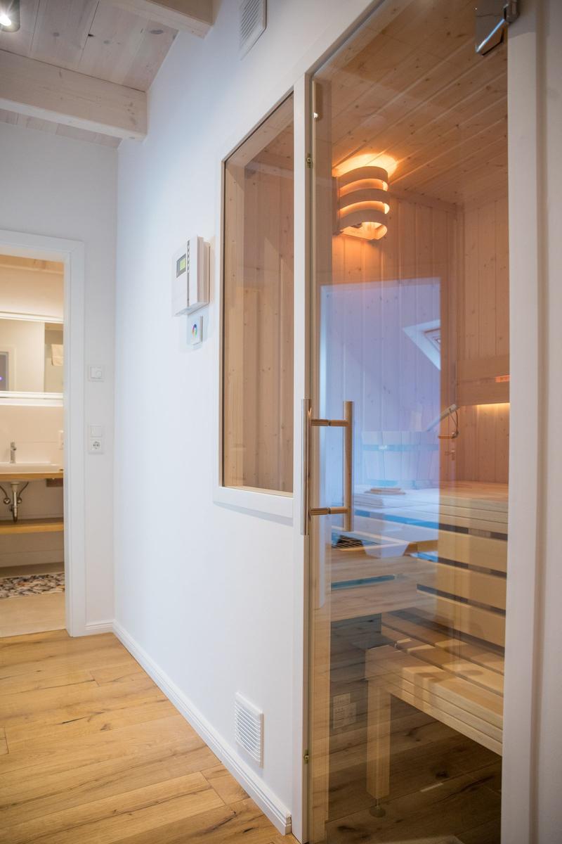 Sauna mit Holzbank und Glaswand. Nebenraum mit Waschbecken und Spiegel.