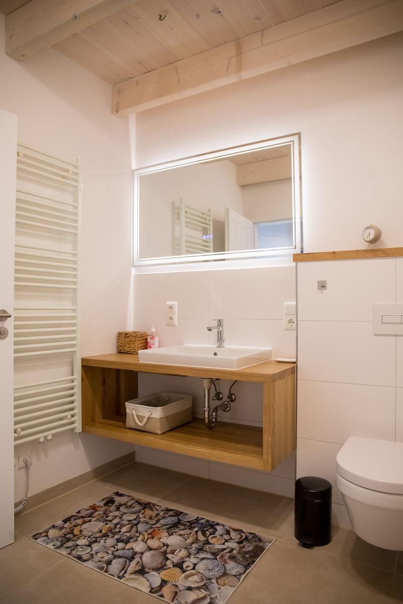 Badezimmer mit Holzwaschtisch, Spiegel und Marmorfliesenboden. Dampfbad und Toilette sind vorhanden.