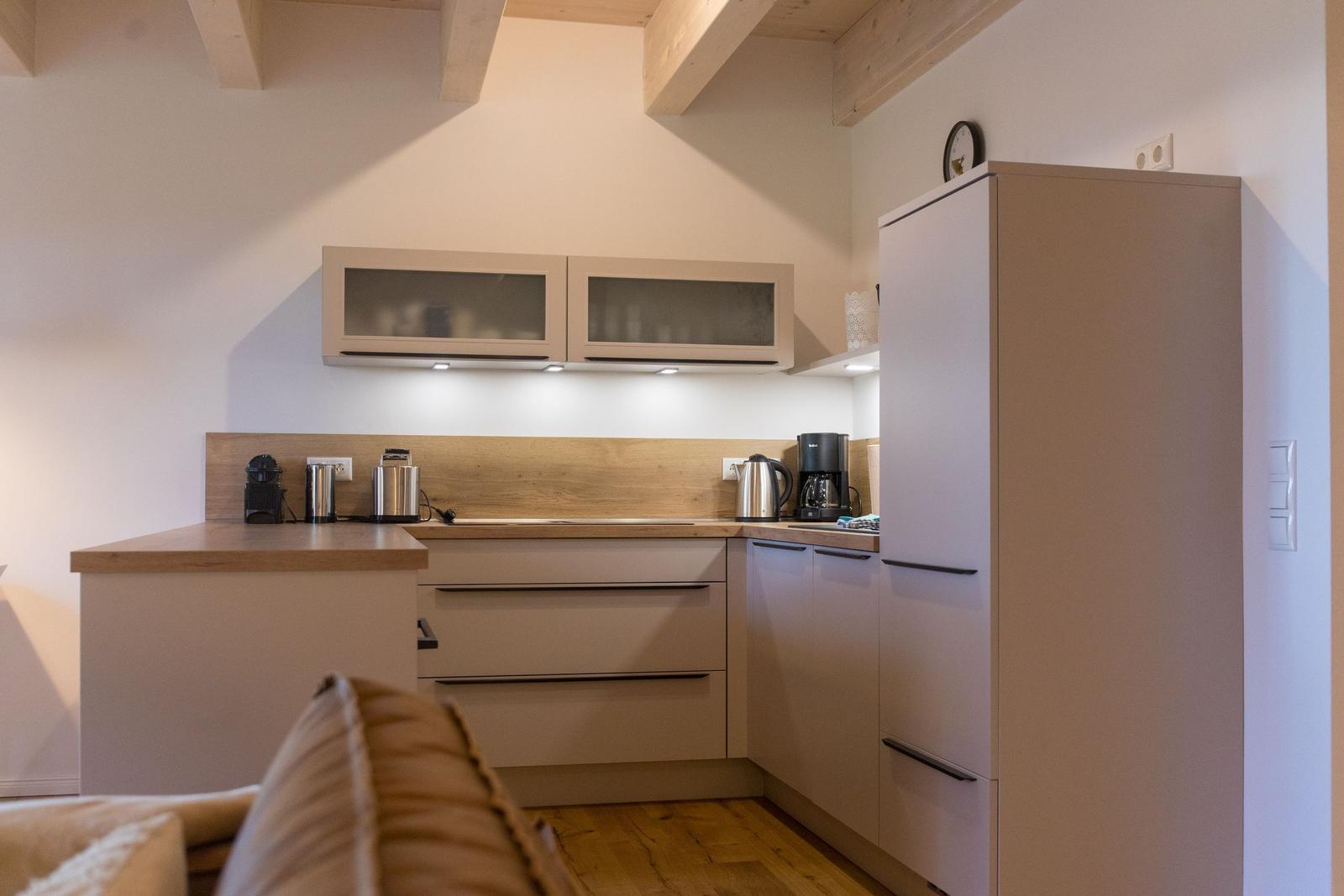 Küche mit Holzoberfläche, Schränken und Kühlschrank. Holzdeckenbalken sichtbar.