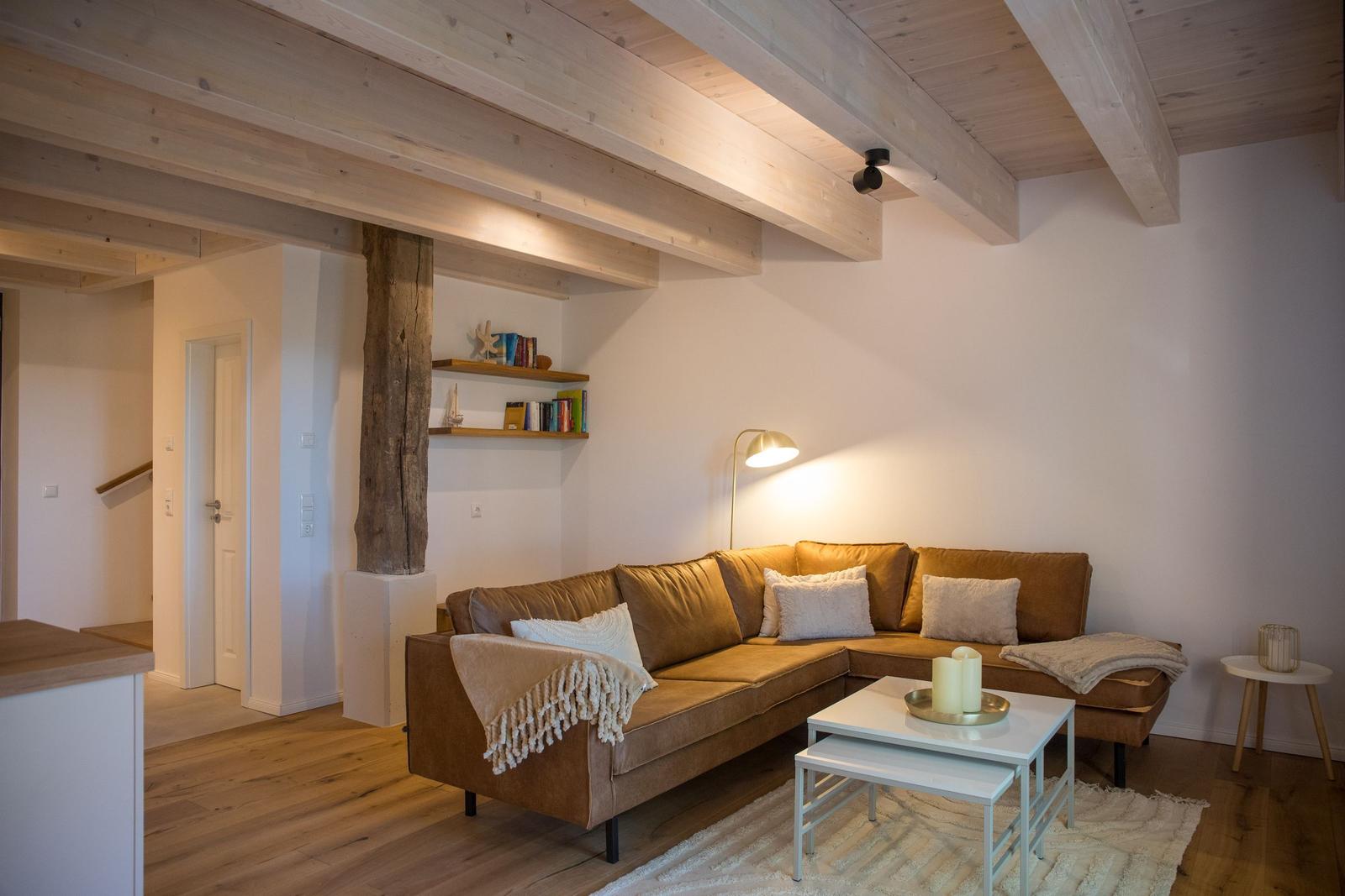 Wohnzimmer mit braunem Sofa, Holzbalken und weißem Tisch.