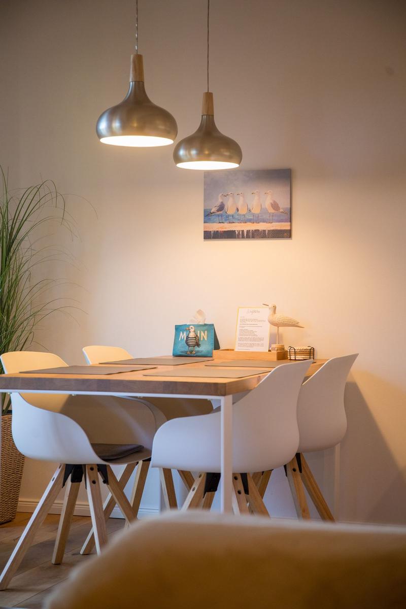 Esstisch mit weißen Stühlen und zwei Hängelampen an der Wand.