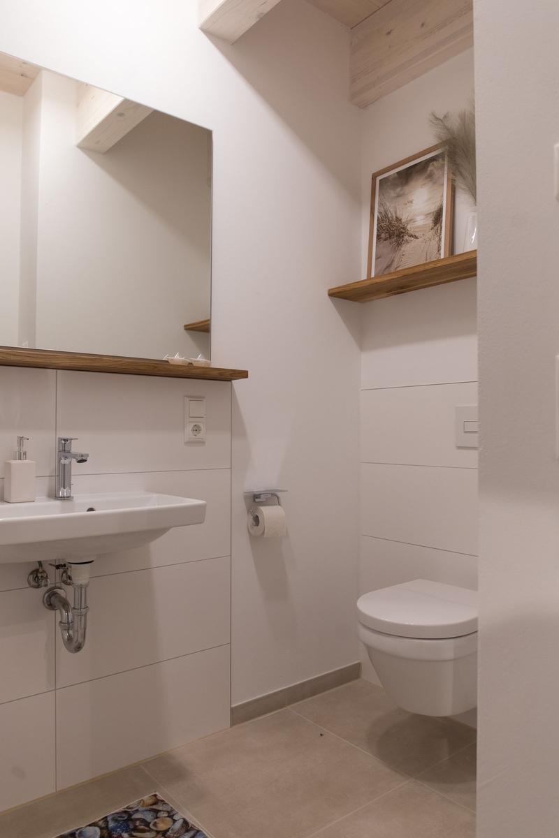 Badezimmer mit Waschbecken, Spiegel, Toilette und Holzregal.