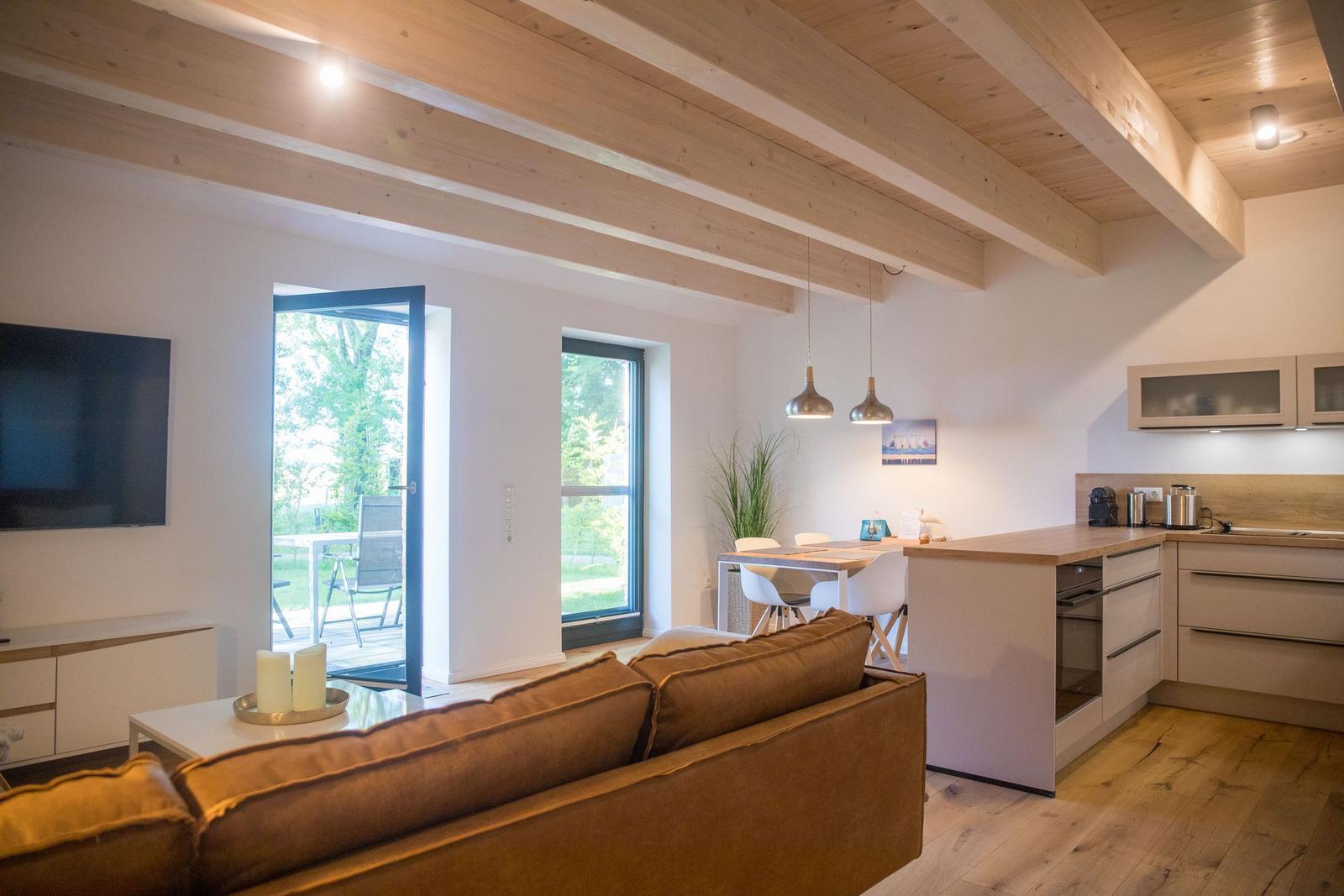 Wohnküche mit Holzbalkendecke, Sofa, TV und Terrasse. Moderne Einrichtung.