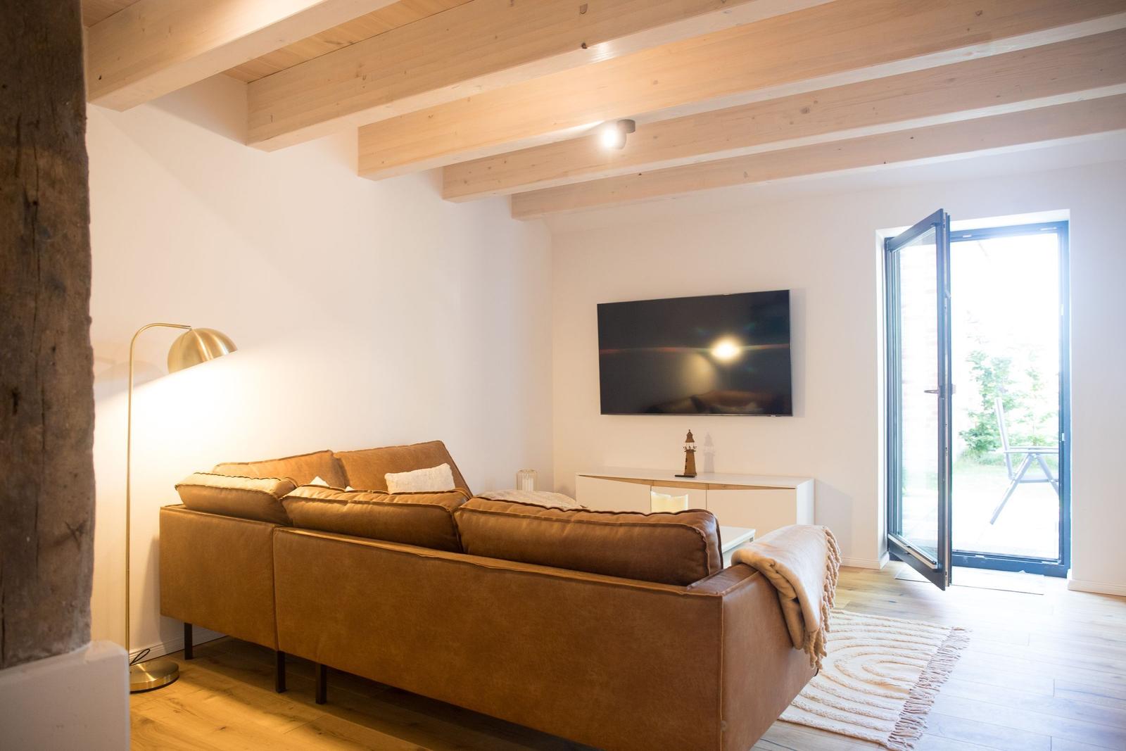 Wohnzimmer mit braunem Sofa, Fernseher und Terrassentür.