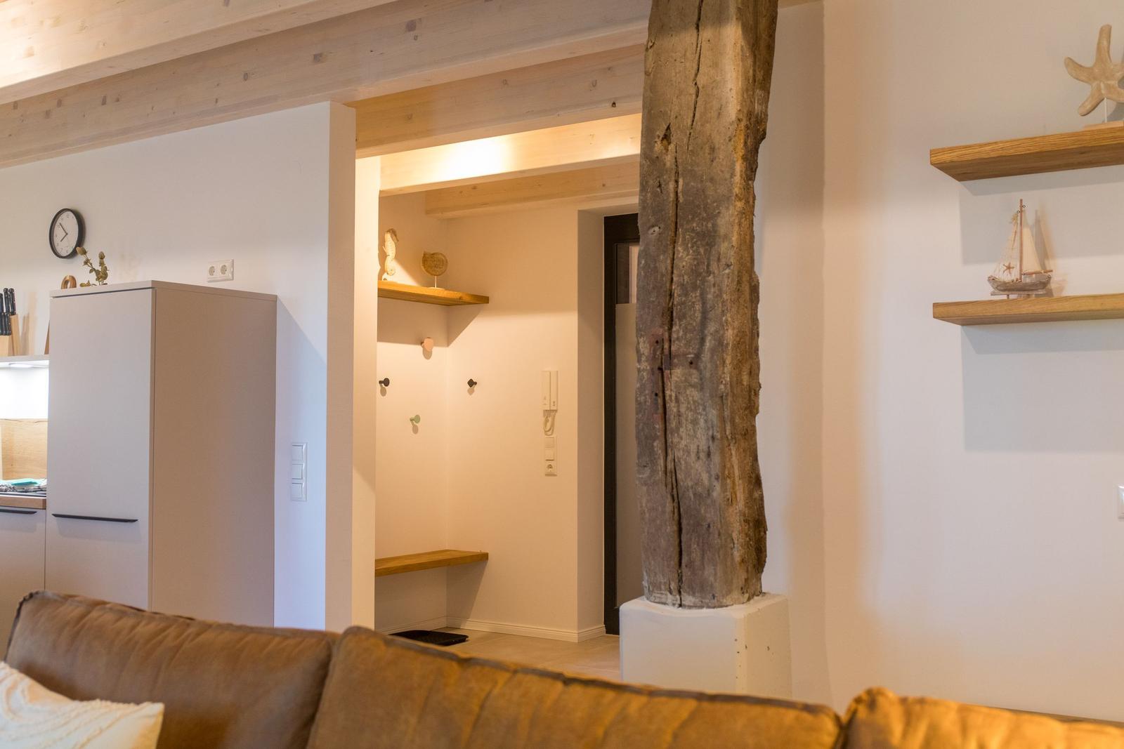 Wohnbereich mit Sofa, Küchenzeile und massivem Holzpfosten. Regale mit Schiffmodell und Stern.