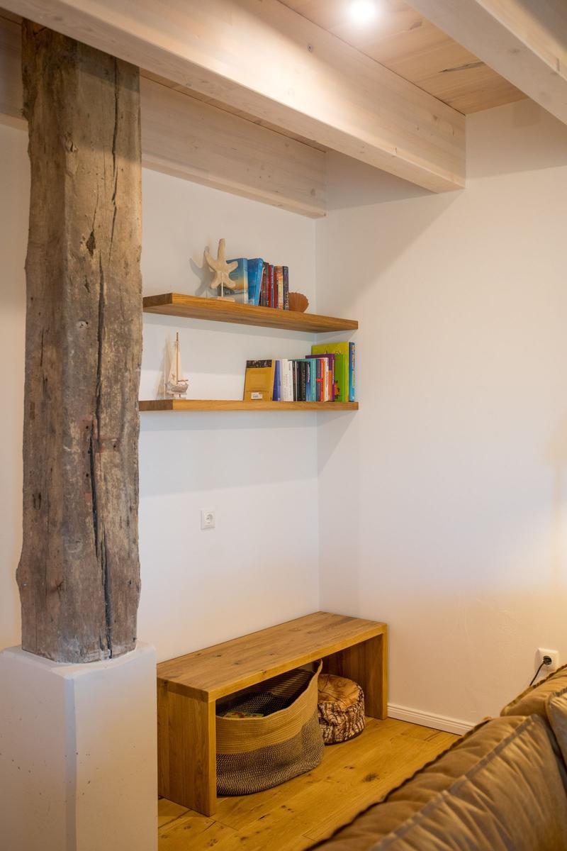 Raum mit Holzbalken, Regalen, Bank und Kissen. Holzfußboden und weiße Wände.