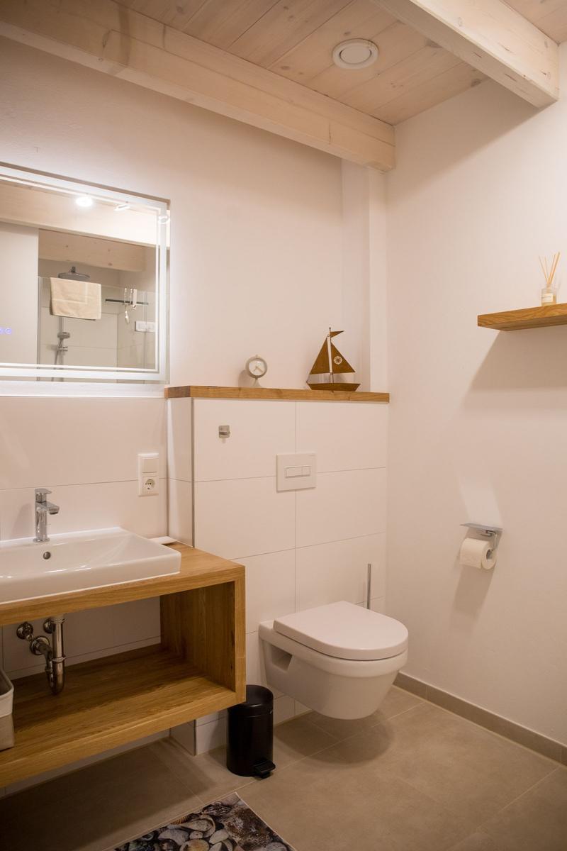 Badezimmer mit Waschbecken, Toilette und Spiegel. Holzakzente und Dachbalken.