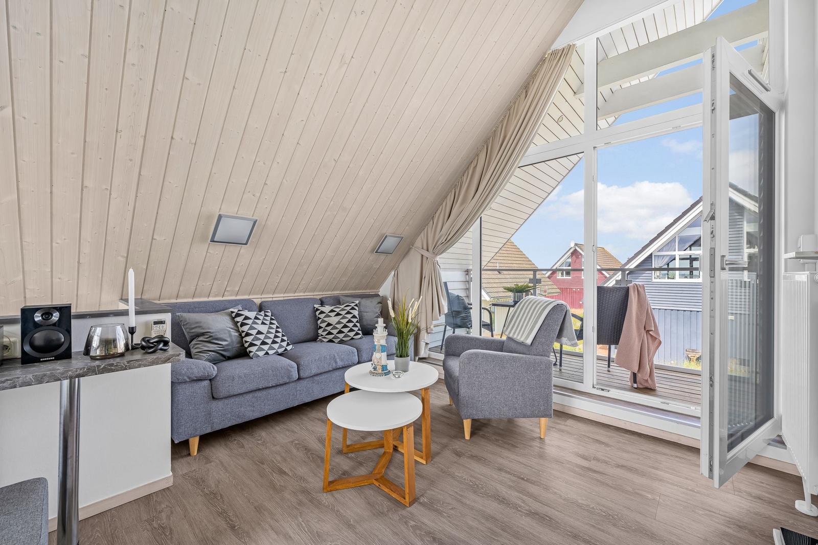 Wohnzimmer mit Sofa, Sessel und Balkonzugang.