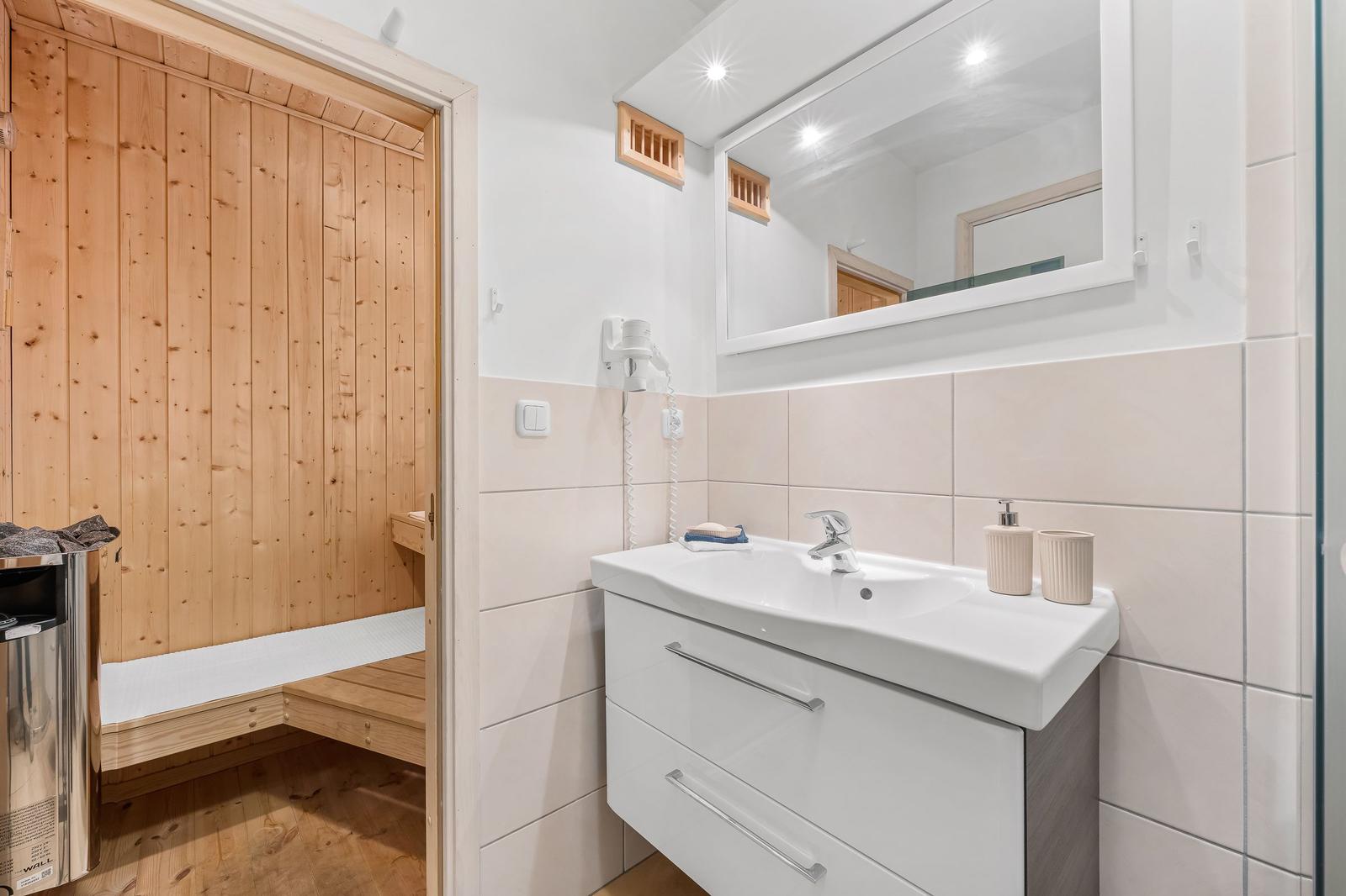 Badezimmer mit Waschbecken, Spiegel und Blick in die Sauna.