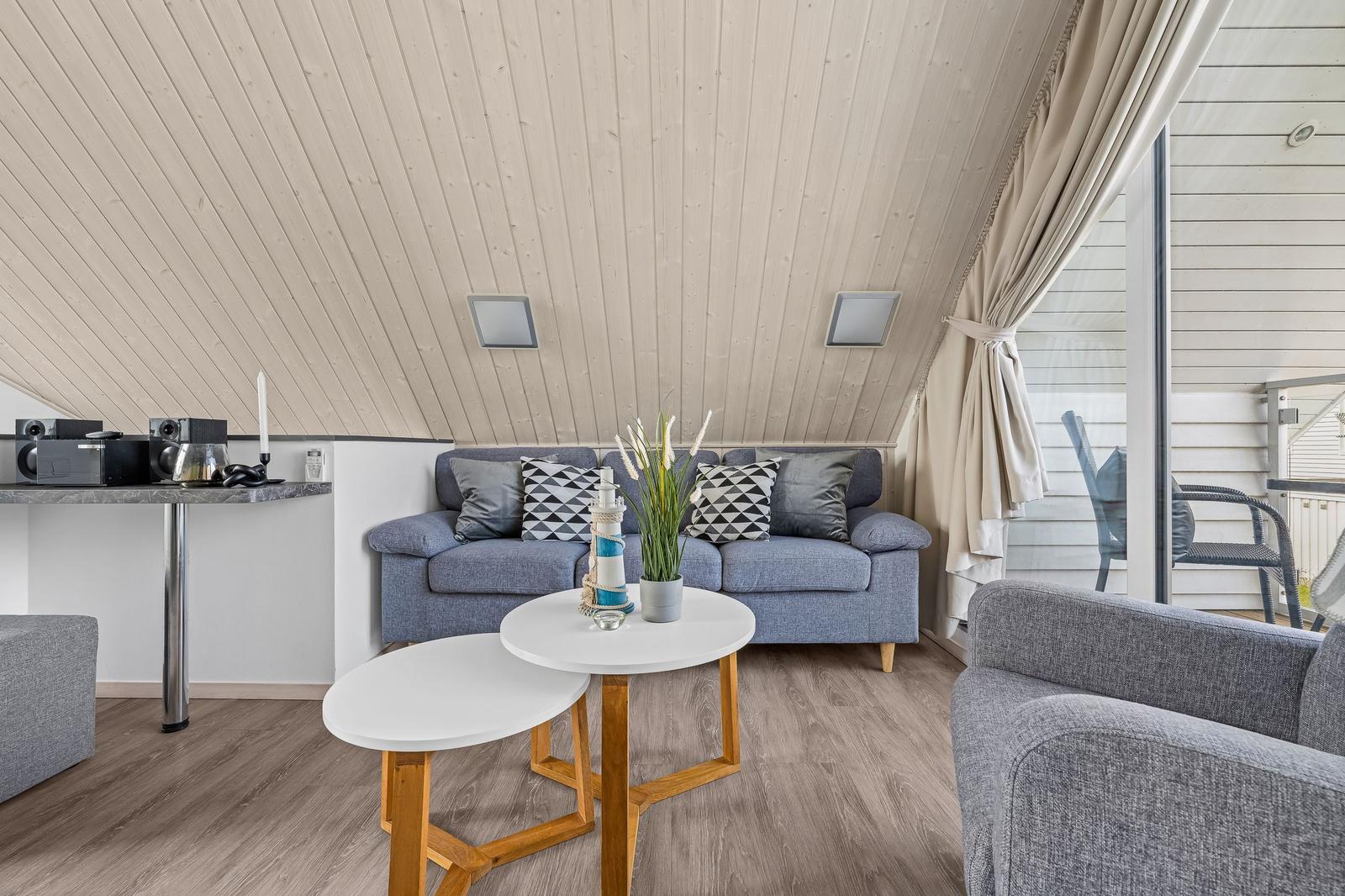 Wohnzimmer mit Sofa, Tischen und Balkonzugang.