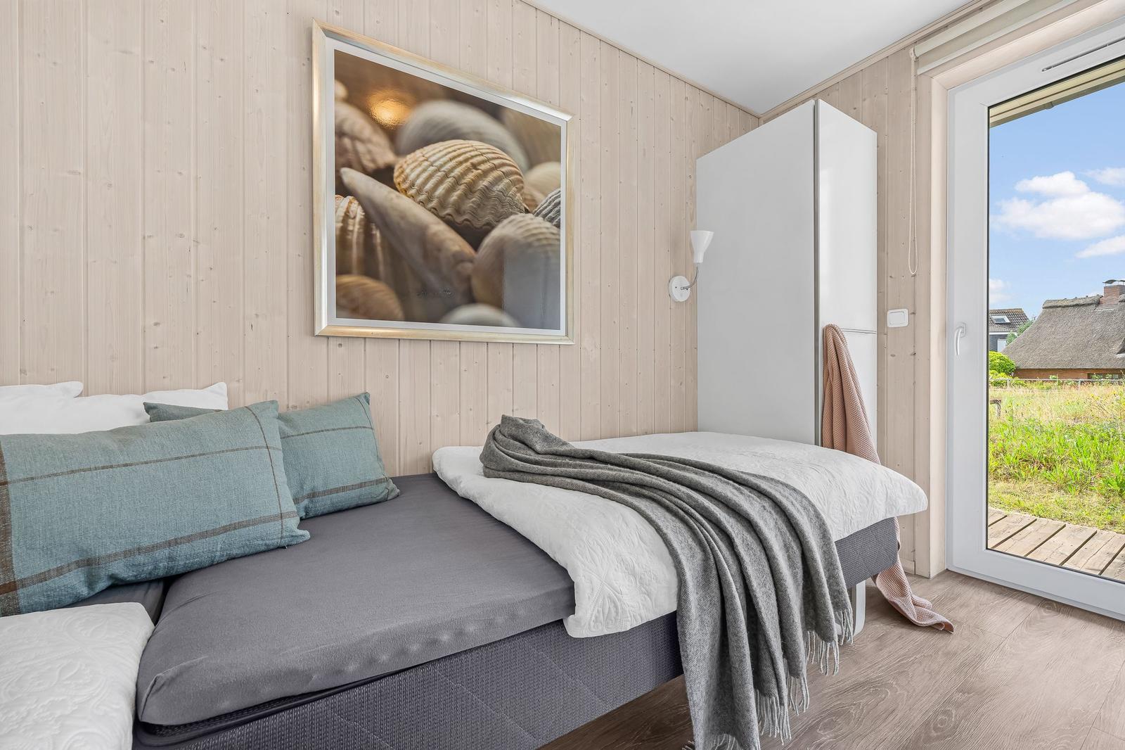 Schlafzimmer mit Bett, Wandbild und Glastür zum Garten.