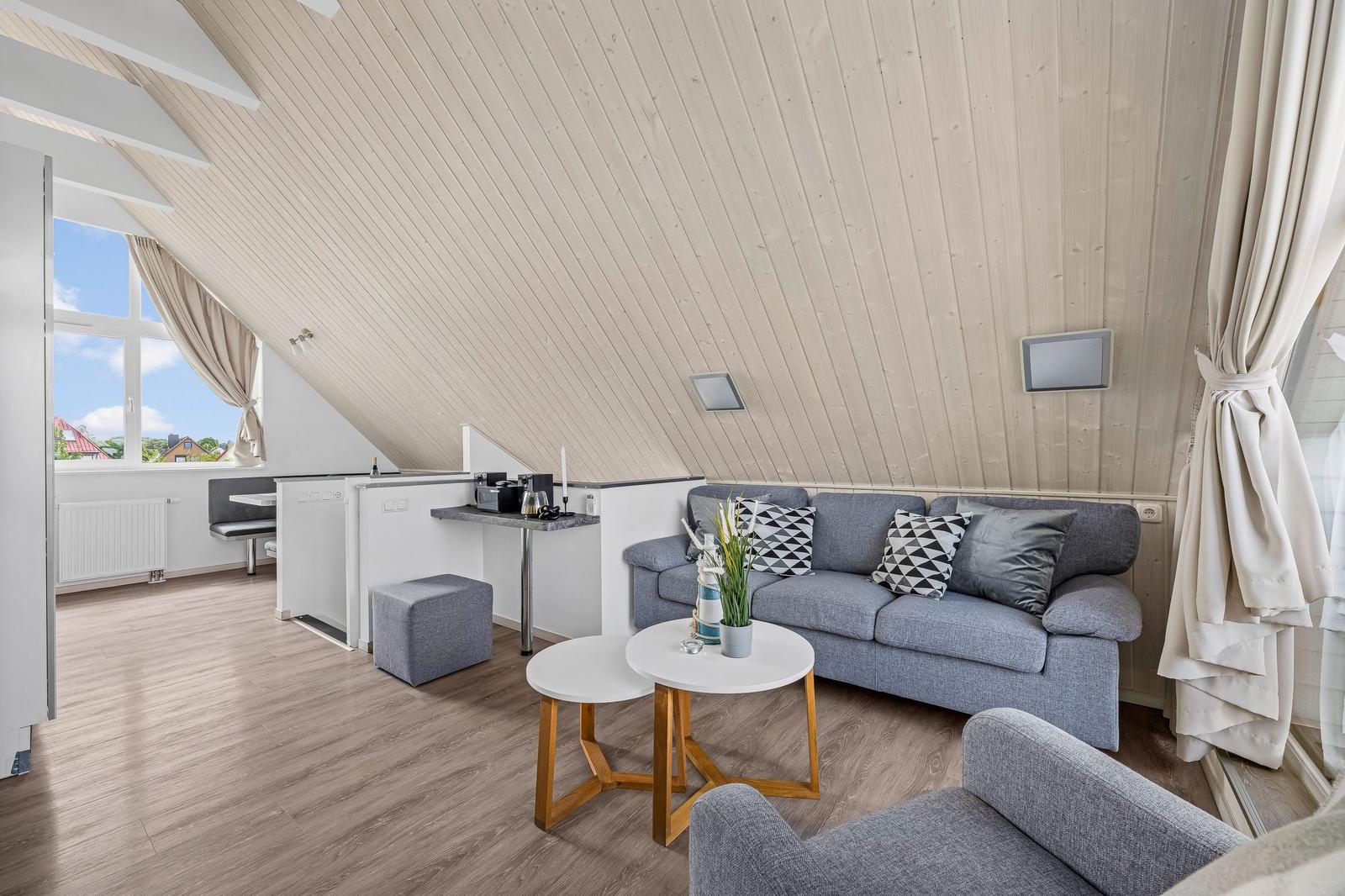 Wohnraum mit Sofa, Tisch und Blick aus Fenster. Holzdecke und Parkettboden.